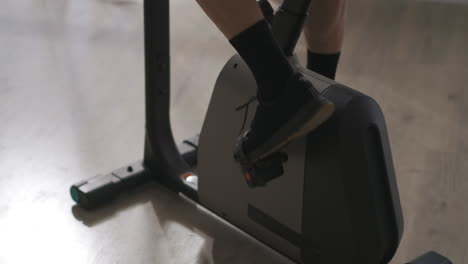legs-of-elderly-man-on-pedals-of-stationary-bike-indoors-closeup-view-training-at-home-healthy-lifestyle-sport-activity-in-old-age